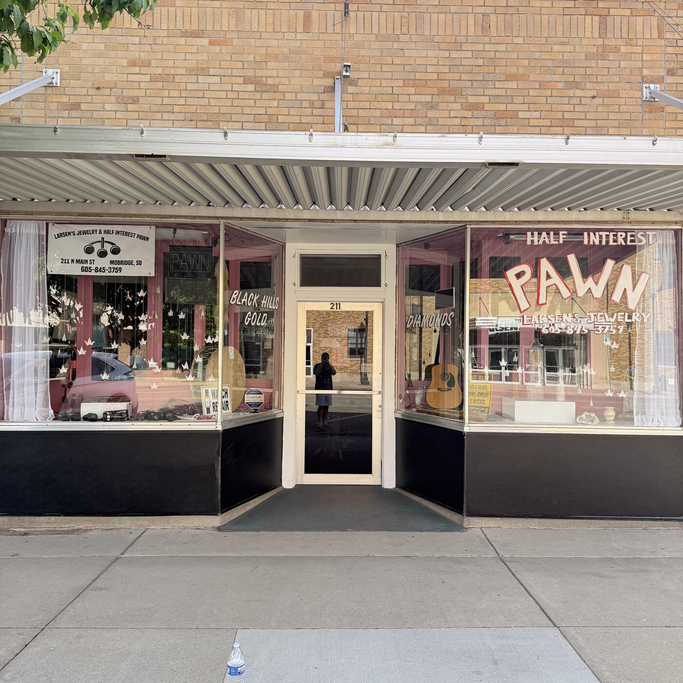 Storefront of Larsen&rsquo;s Jewelry & Half Interest Pawn at 211 N Main Street in Mobridge, South Dakota, with hand-painted &lsquo;Half Interest Pawn&rsquo; lettering, a &lsquo;Black Hills Gold&rsquo; window, and small signs for Diamonds and Watch Repair.